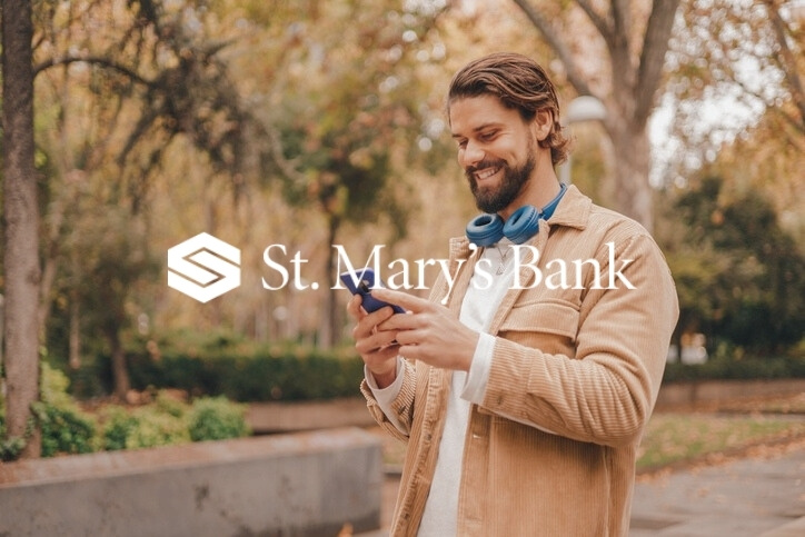 man using cellphone in a park with St. Mary's Bank logo overlayed