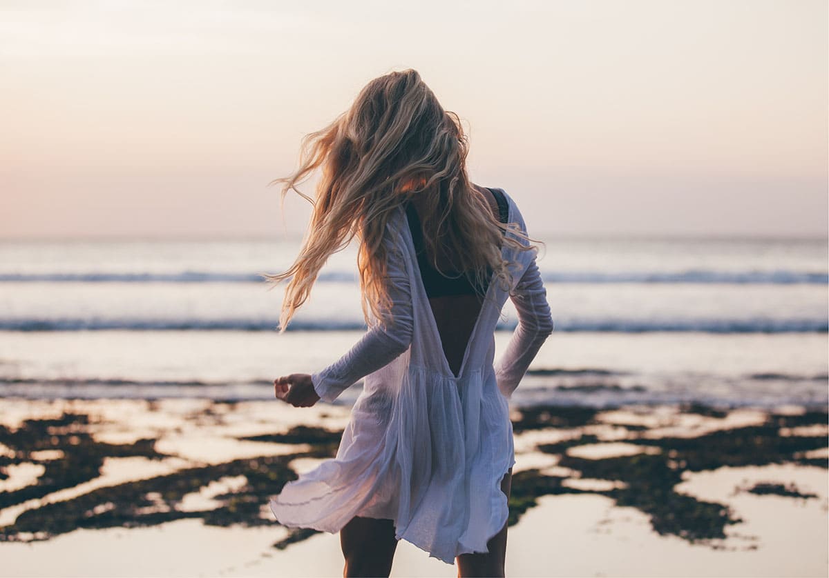 woman in a white dress walking on the beach towards the ocean